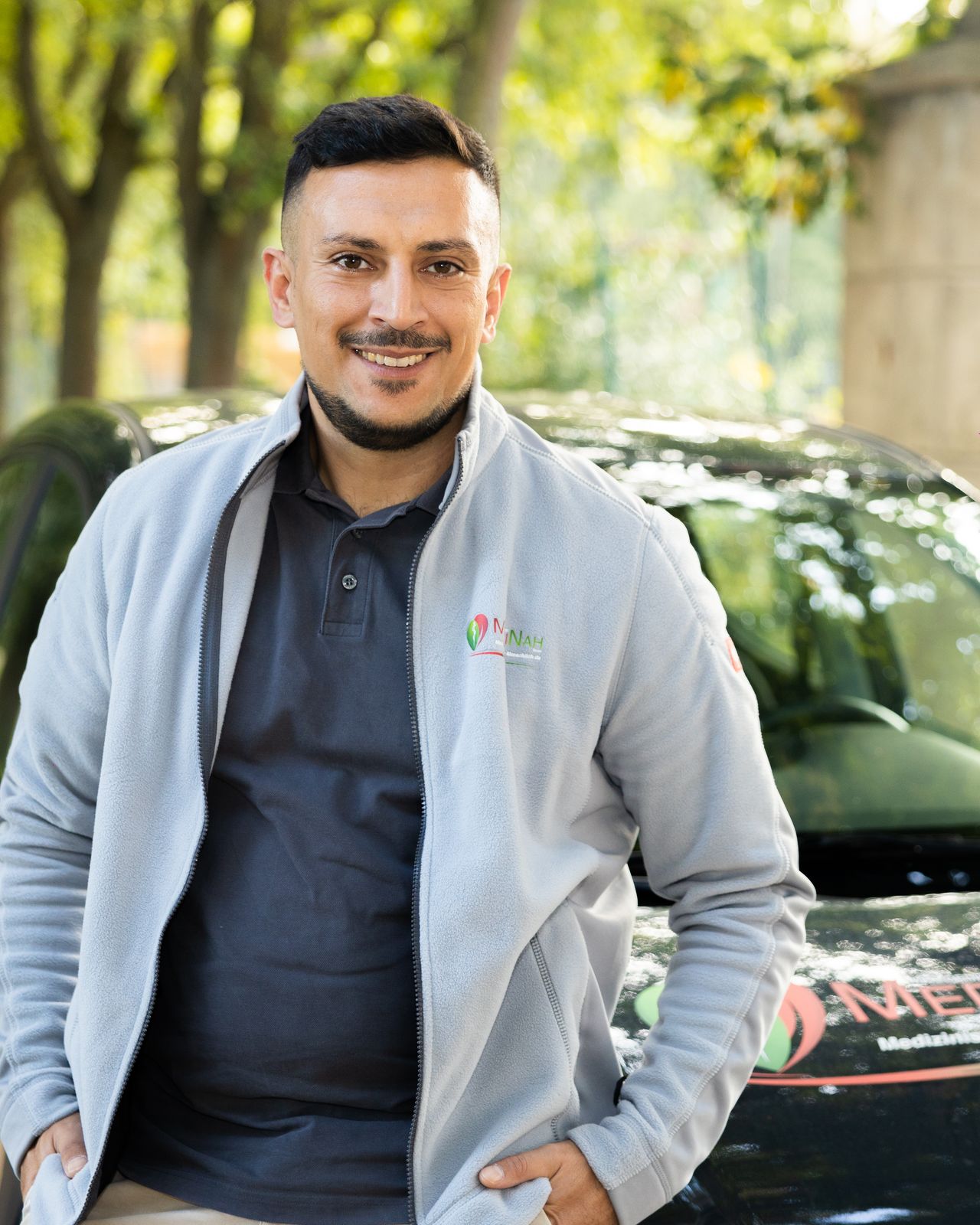 Mitarbeiter lehnt lächelnd am Firmenwagen mit MediNah-Logo